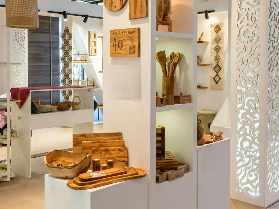 ArtisRaw's olive wood display at Maison&Objet Paris 2026: cutting boards, a carved serving bowl, nested serving trays and utensils in a holder around the engraved ArtisRaw sign