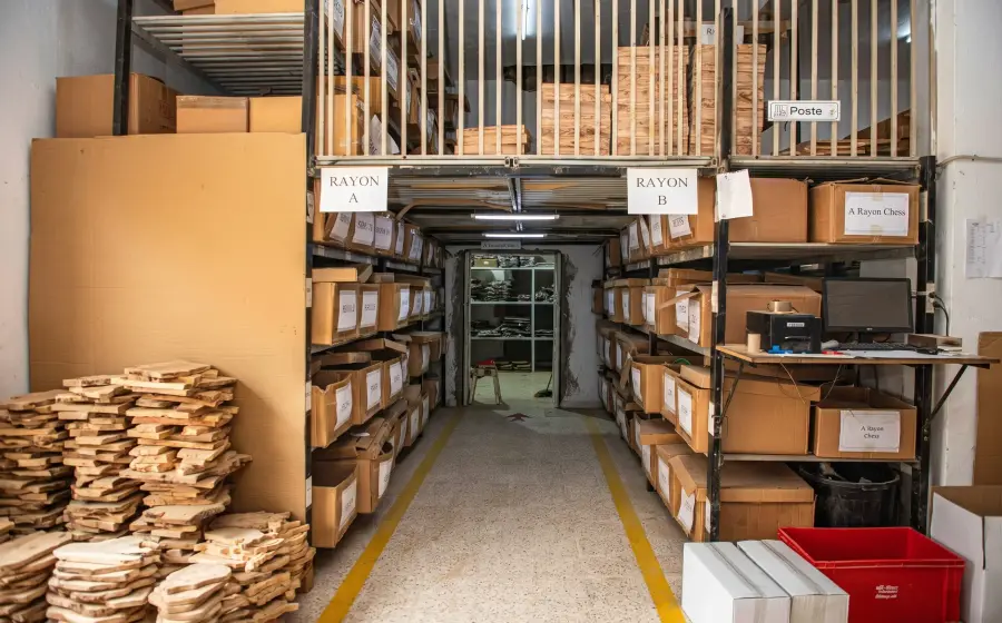 The ArtisRaw finished-goods store in Sfax: aisles of racking labelled Rayon A and Rayon B, stacked cartons and olive wood blanks along a taped walkway